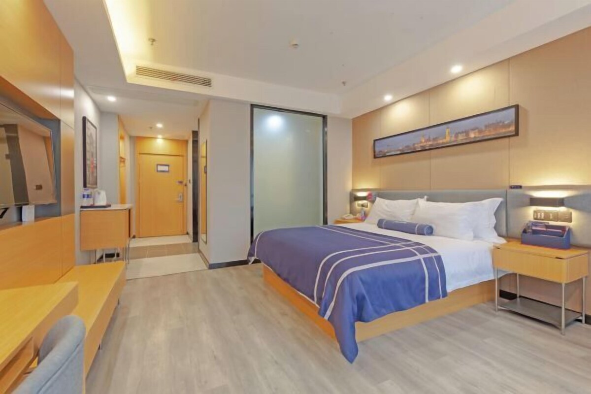 A modern hotel room with a bed, bedside table, and a desk with a chair.