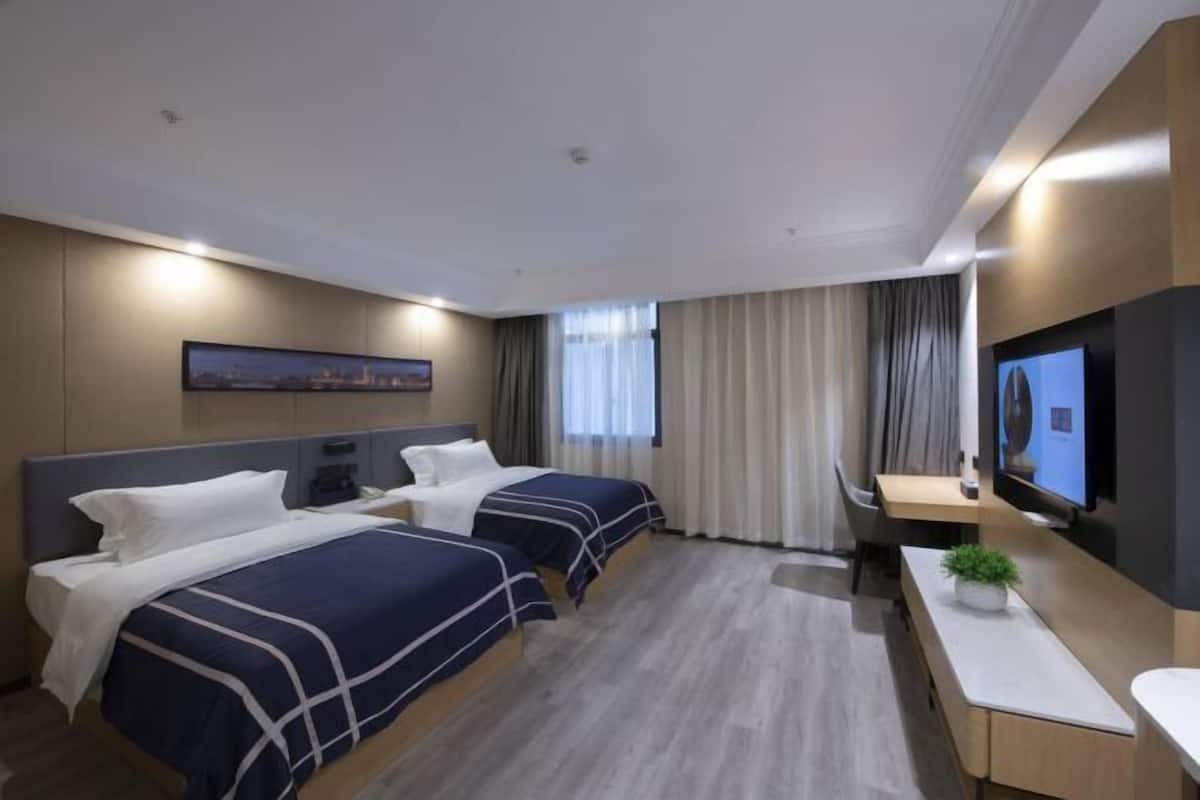 A hotel room with two beds, a desk, a TV, and a window with curtains.