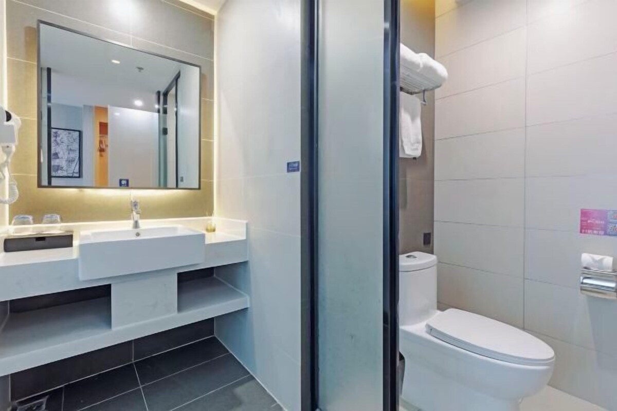 A modern bathroom with a large mirror, a sink, a toilet, and a glass shower enclosure.