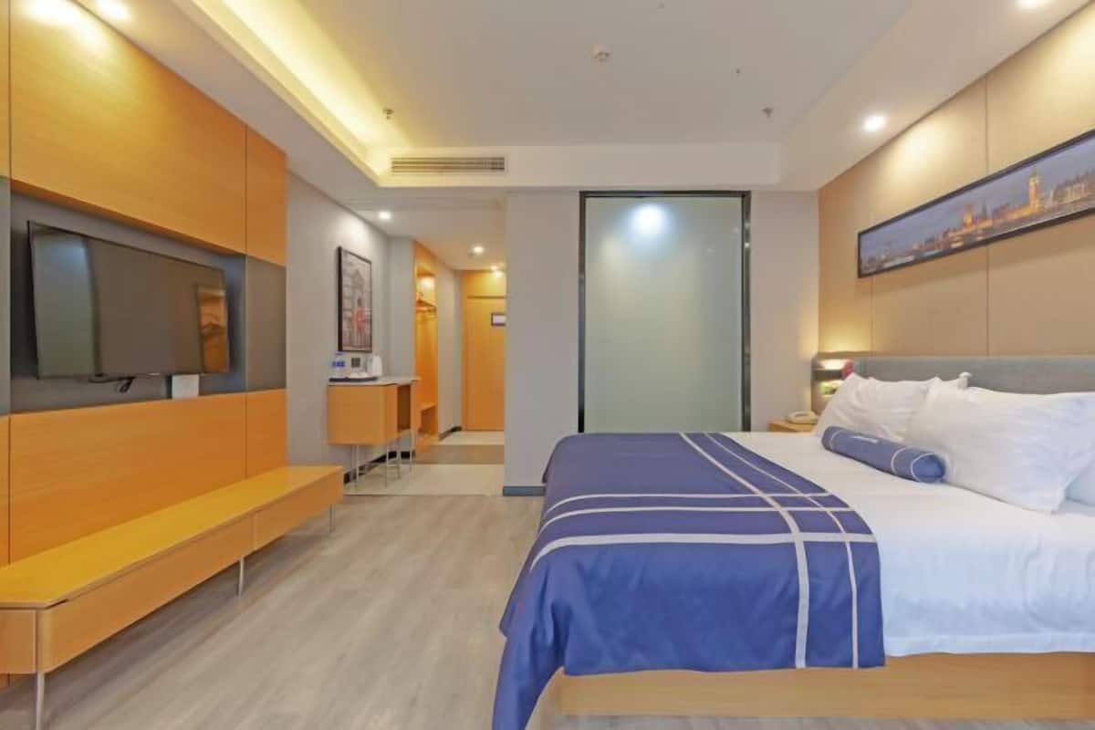 A hotel room with a bed, a bench, a TV, and a painting on the wall.