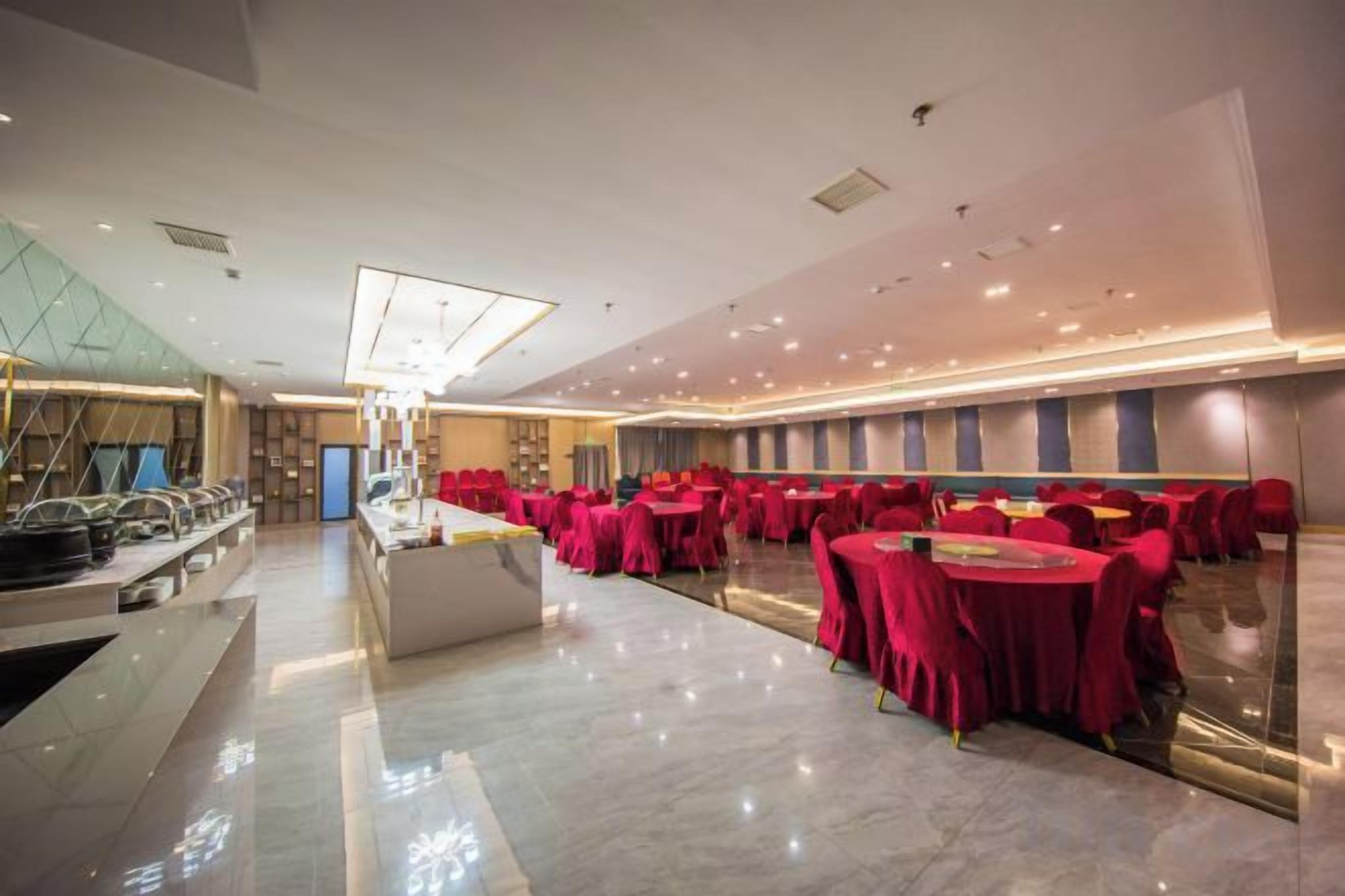 Un espacioso salón de banquetes con mesas redondas cubiertas con manteles rojos, una isla central con una lámpara y una decoración interior moderna.