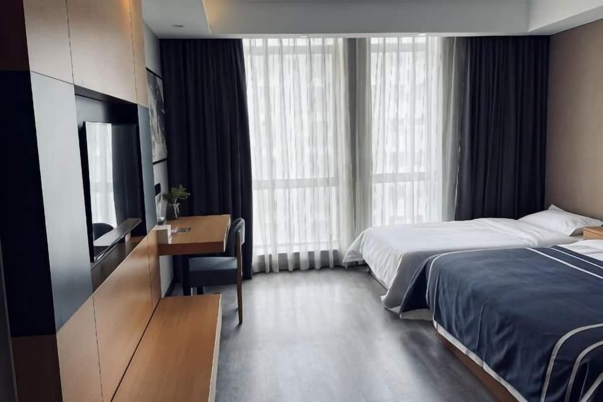 A hotel room with a bed, a desk, a TV, and large windows with curtains.