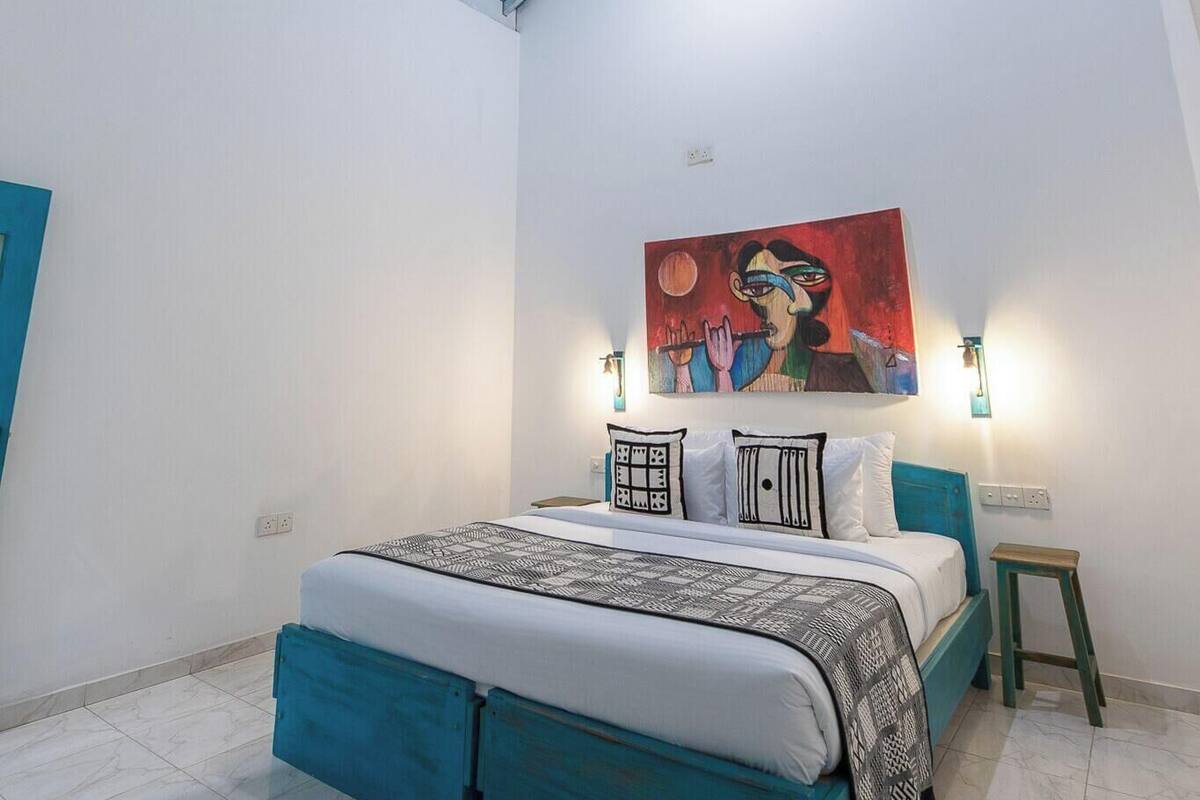 Een slaapkamer met een bed, een schilderij en een plafondventilator.