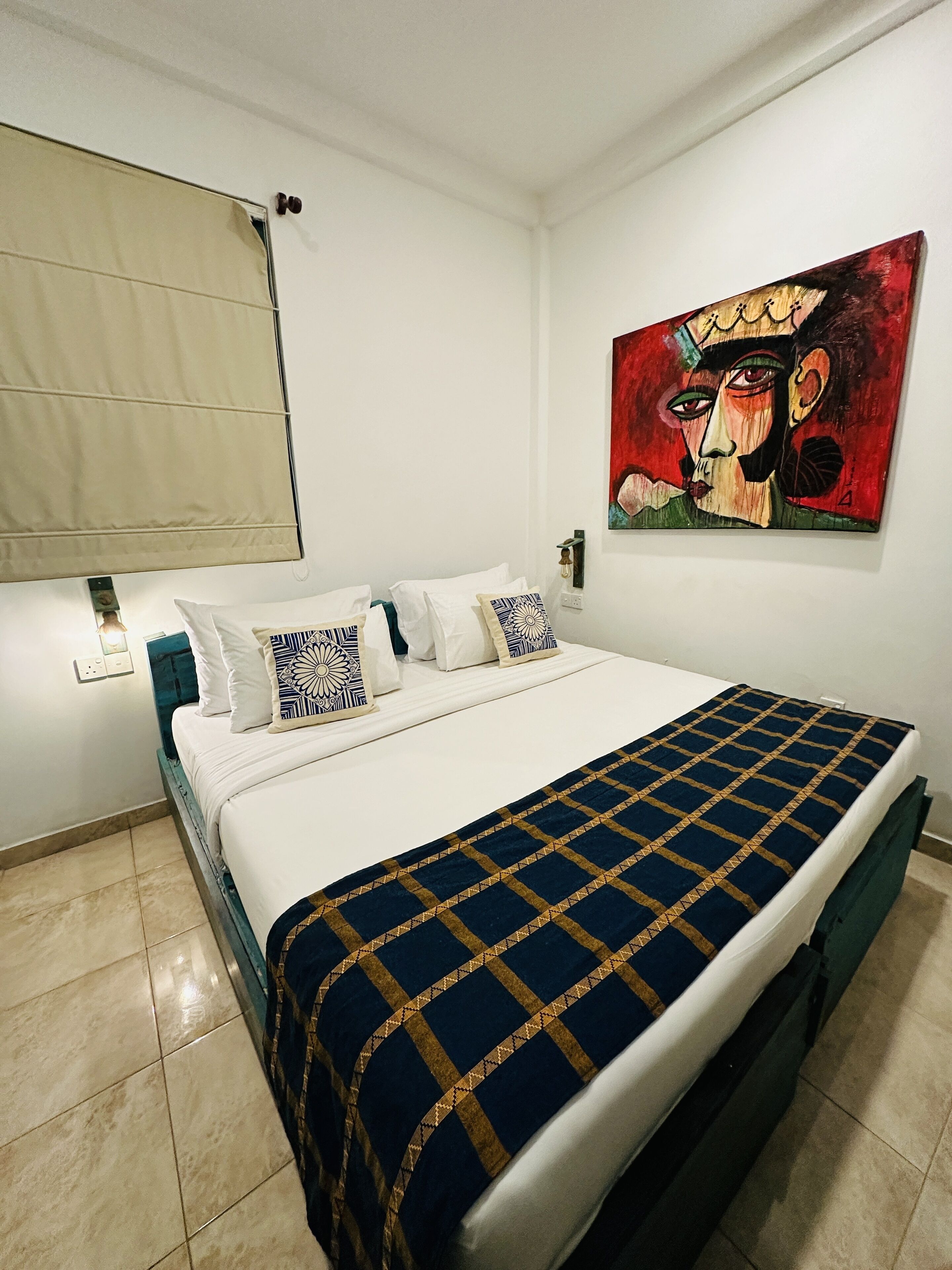 A neatly made bed with patterned pillows, a blue and gold checkered bedspread, and a painting on the wall.
