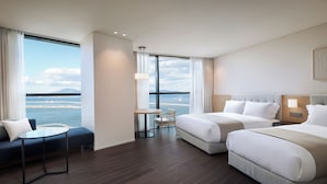 Een hotelkamer met twee bedden, een bank, een tafel en uitzicht op zee.