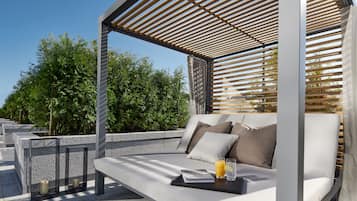 A modern outdoor seating area with a cushioned bench, a glass table with a drink, and a wooden pergola structure.