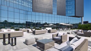 Een dakterras met buiten zitplaatsen, parasols en uitzicht op een modern gebouw.