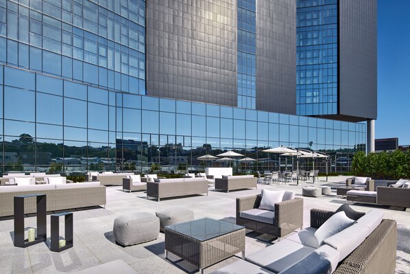 Terraza en la azotea con asientos al aire libre, sombrillas y vistas de un edificio moderno.