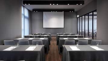 A conference room with tables, chairs, a projector screen, and large windows.