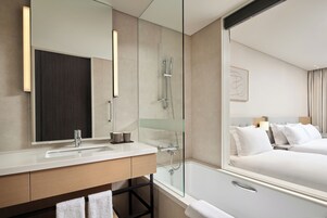 Un baño de hotel moderno con un espejo grande, un lavamanos, una ducha y una bañera.