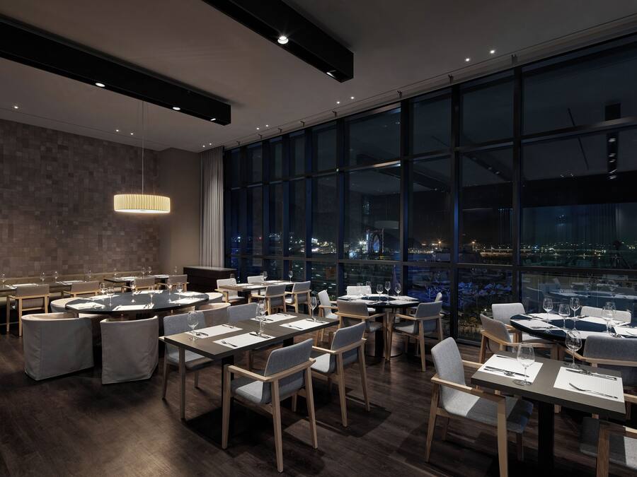 A modern dining area with tables and chairs, large windows offering a city view, and a contemporary pendant light.