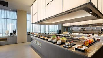 Un bufé de desayuno moderno con gran variedad de alimentos y bebidas, un amplio ventanal que proporciona luz natural y un diseño limpio y contemporáneo.