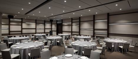 Un salón de conferencias con varias mesas redondas, cada una dispuesta con platos, cubiertos y vasos.