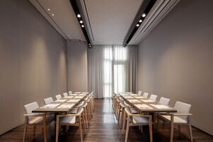 Un salón de conferencias con una larga mesa y sillas, ventanas amplias con cortinas e iluminación empotrada en el techo.