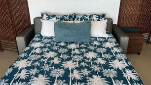 A bed with a blue and white palm tree bedspread, grey and white pillows, and a grey headboard. - Sandstone Point Family home, Bribie beaches, pet friendly  (Sandstone Point)