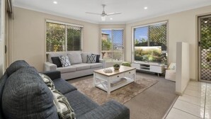A modern living room with a grey sofa, a white coffee table, and a ceiling fan. - Sandstone Point Family home, Bribie beaches, pet friendly  (Sandstone Point)