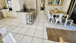 A modern kitchen with white cabinets, a black countertop, and a built-in oven. There is a dining area with a wooden table and white chairs. - Sandstone Point Family home, Bribie beaches, pet friendly  (Sandstone Point)