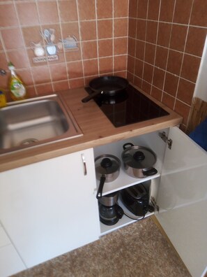 A kitchen with a sink, a stove, and a cabinet with pots.