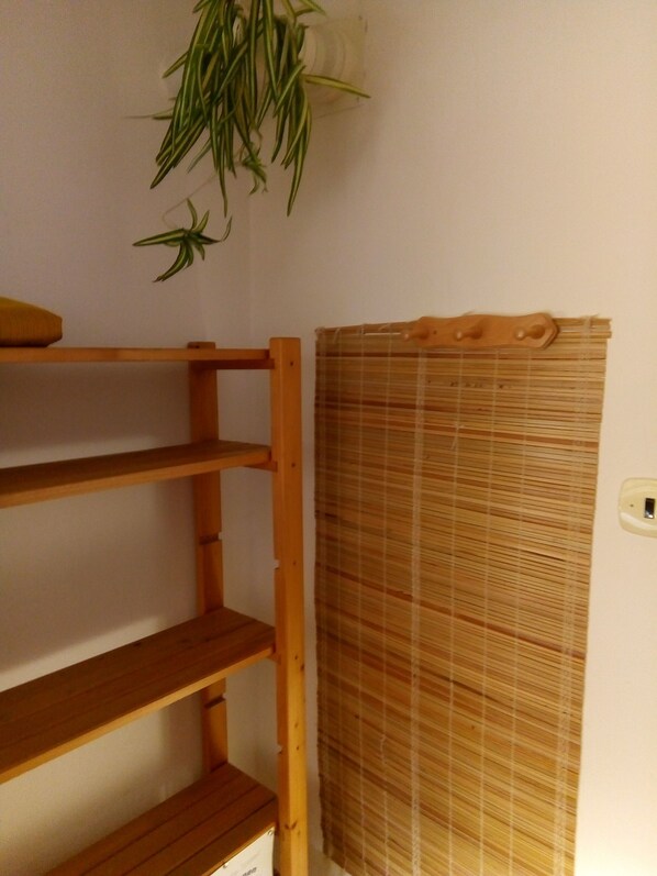 A room with a wooden shelf unit, a bamboo blind, and a hanging plant.