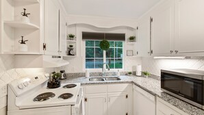 Una cucina moderna con mobili bianchi, piano cottura integrato, microonde e un'ampia finestra vista verde.