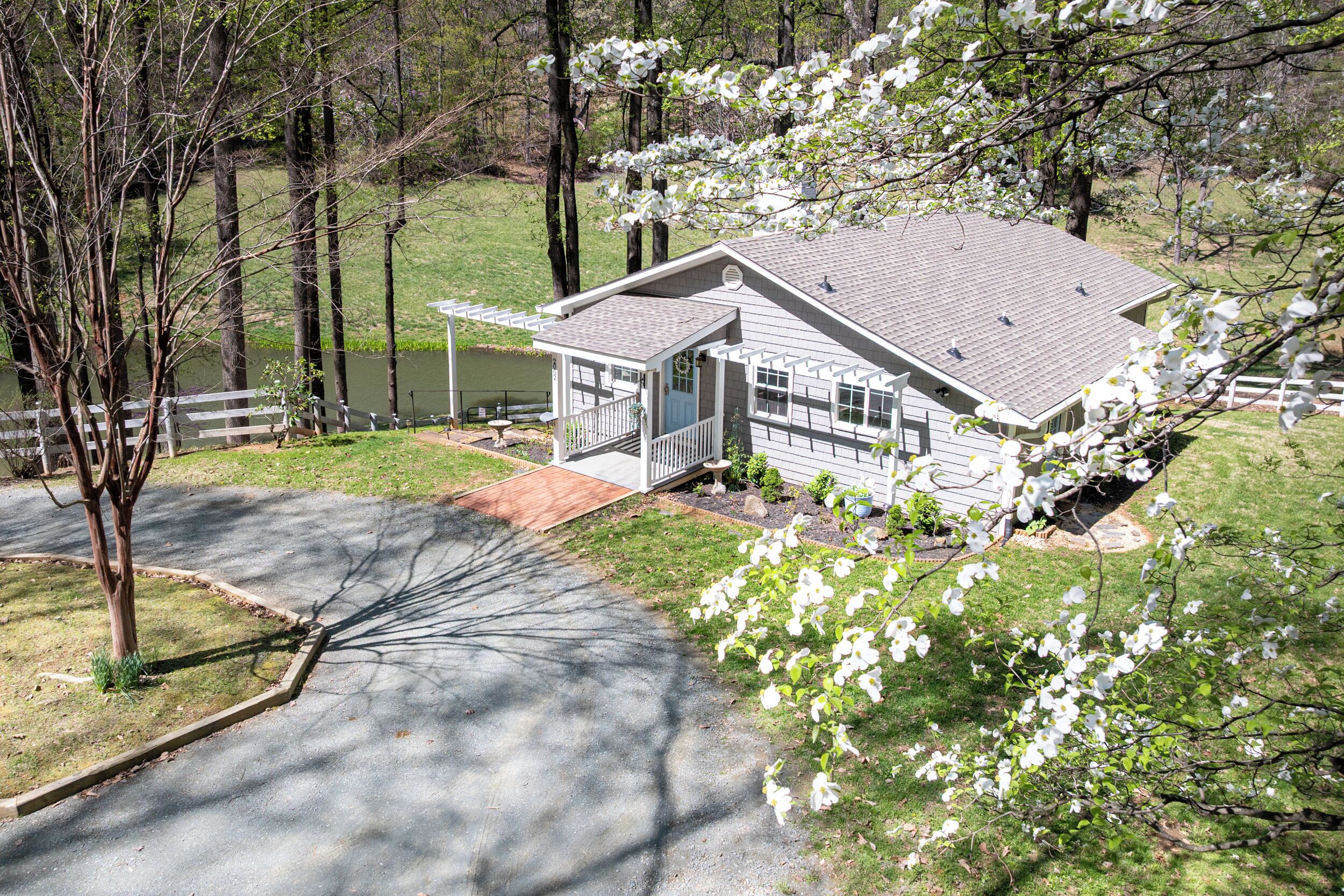 A two-story house with a covered porch, a small deck, and a pond in the background.