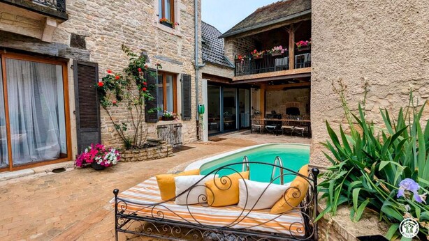 Ein Steinhaus mit Pool, Sitzgelegenheiten im Freien und einem Balkon mit Blumen.