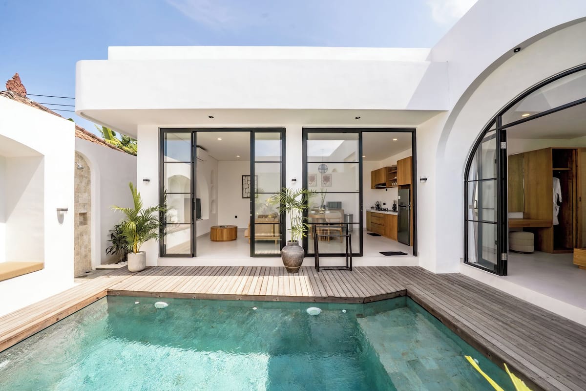 Uma casa moderna com piscina, deck de madeira e grandes portas de vidro que dão para uma cozinha e sala de estar.
