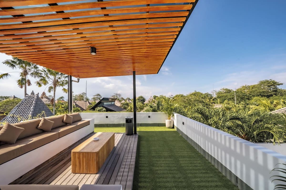 Terraço no telhado com deck de madeira, mobiliário para área externa e vista para o verde ao redor.
