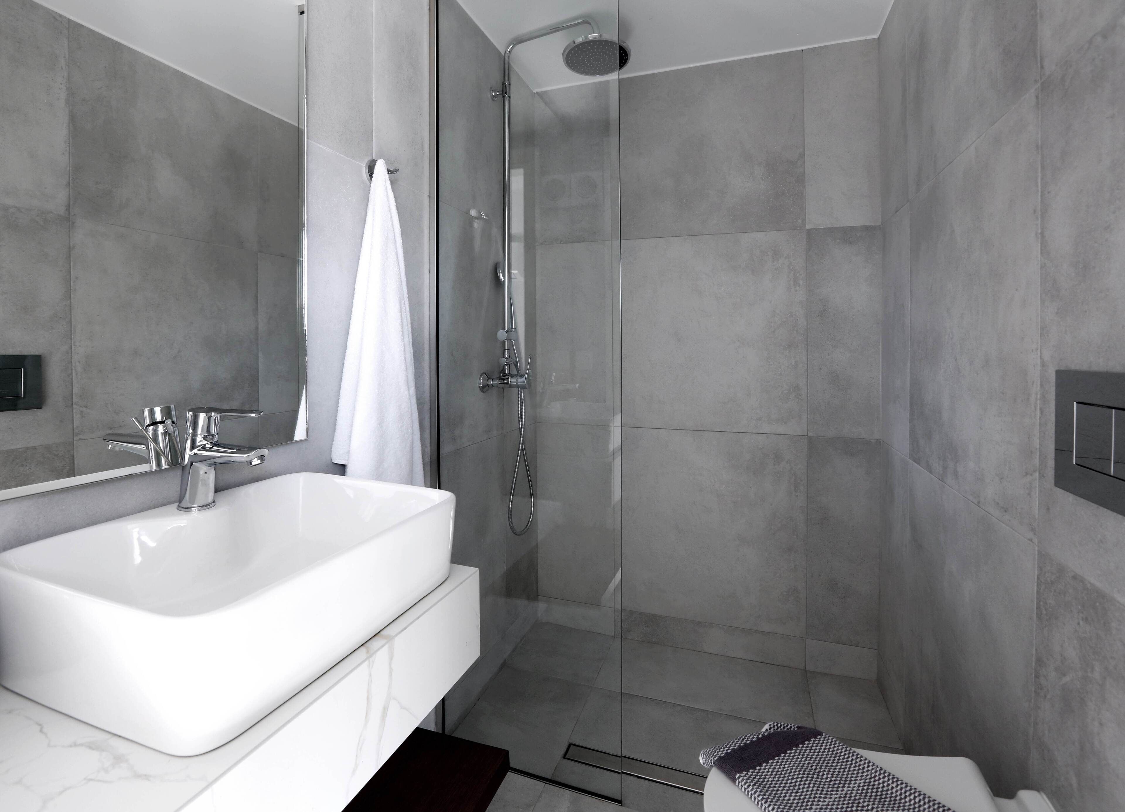 Une salle de bain moderne avec une grande baignoire blanche, une douche à l’italienne et des murs recouverts de carreaux gris.