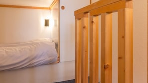 Une chambre de dortoir avec deux lits superposés, une porte en bois et une petite lampe fixée au mur.