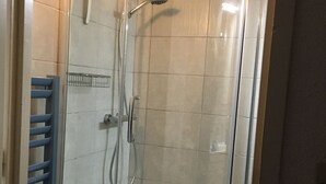 Une douche avec une porte en verre, un pommeau de douche en métal et un porte-serviettes bleu.