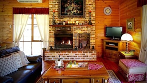 A cozy log cabin interior with a fireplace, a sofa, a television, and a dining table. - Silky Oak Cottage & Studio - Delightful country cottage along popular Hermitage Rd (Pokolbin)