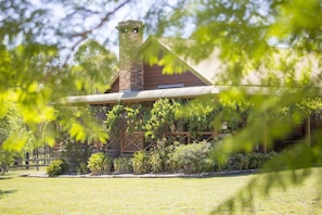 Un bâtiment rustique doté d’une cheminée, entouré d’une végétation luxuriante et d’une pelouse bien entretenue.