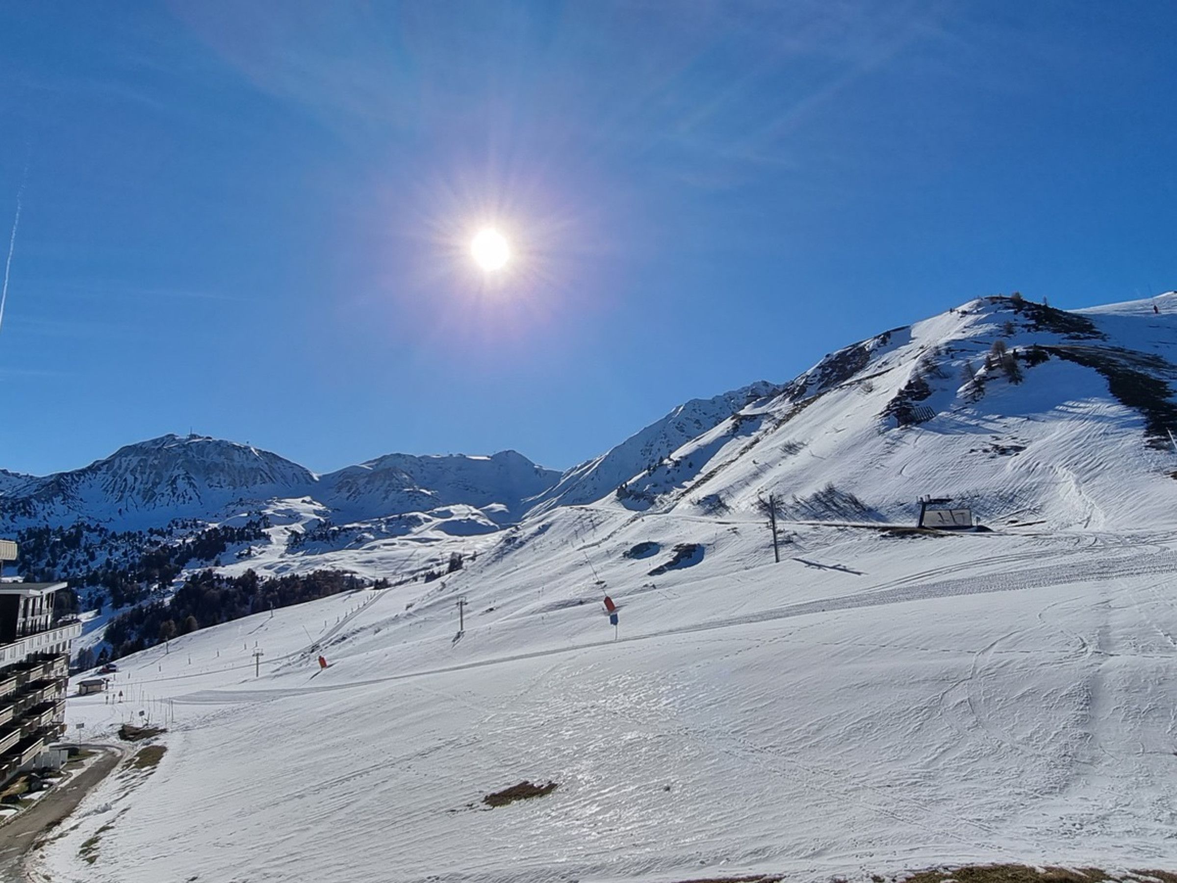 Una pista de esquí cubierta de nieve con cielo despejado y montañas al fondo.