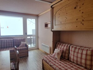 A cozy room with a wooden bench, a sofa with plaid cushions, and a large window offering a view of the outside.