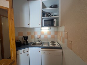 Cocina compacta con armarios blancos, microondas, pileta y lavavajillas.