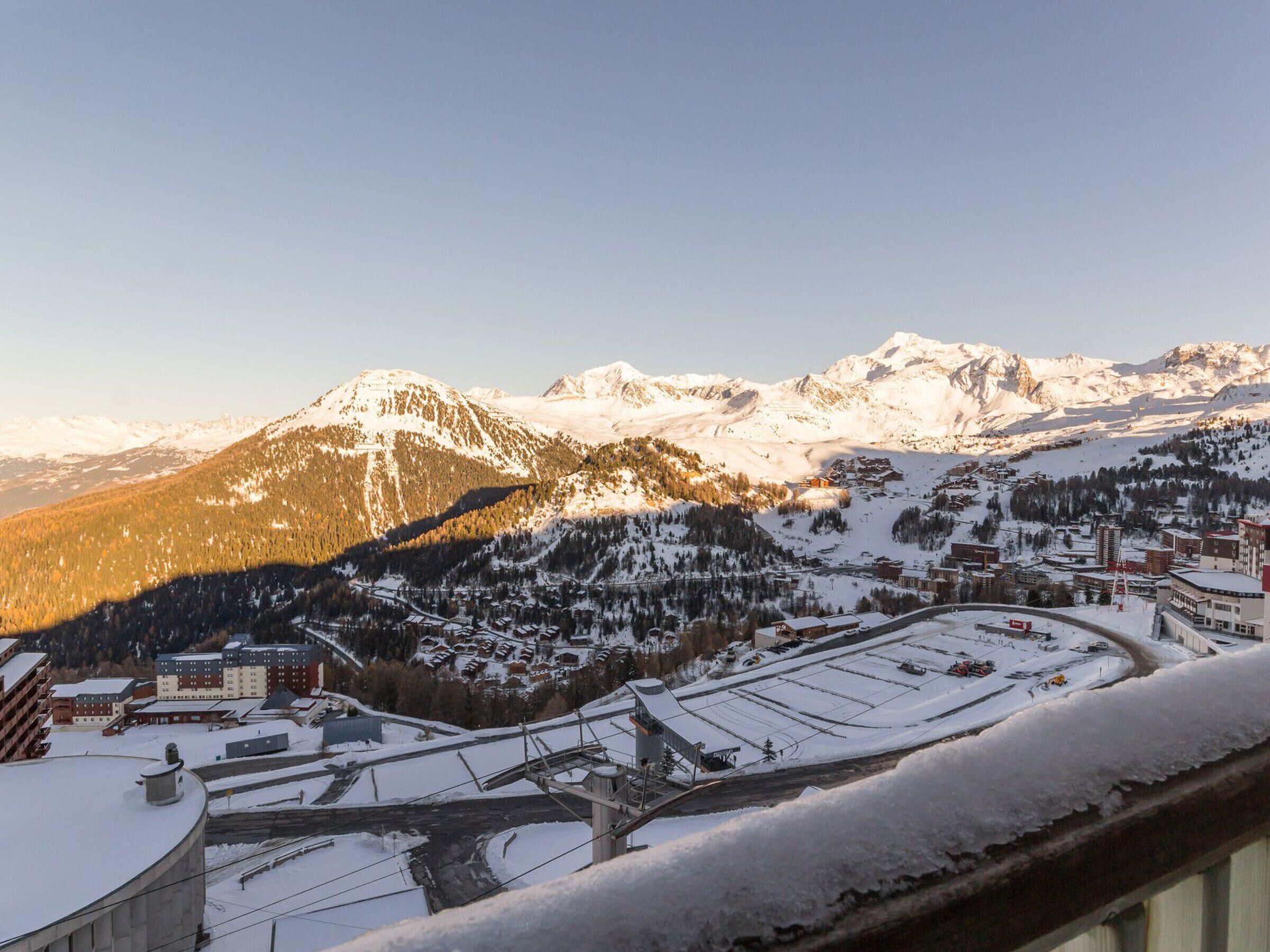 Un pueblo nevado a los pies de una montaña, con edificios y un telesilla.