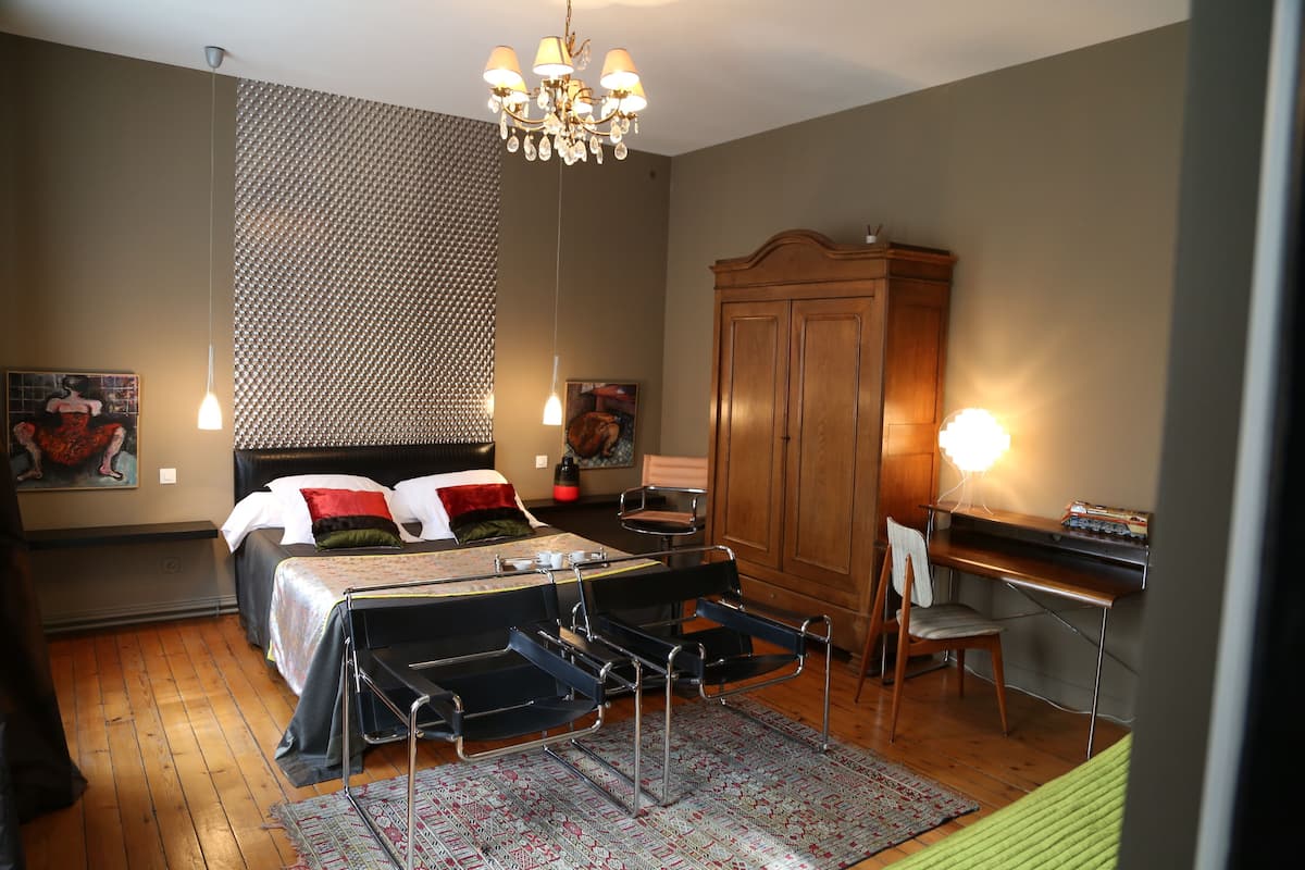 A bedroom with a bed, a desk, a chair, a wardrobe, and a chandelier.