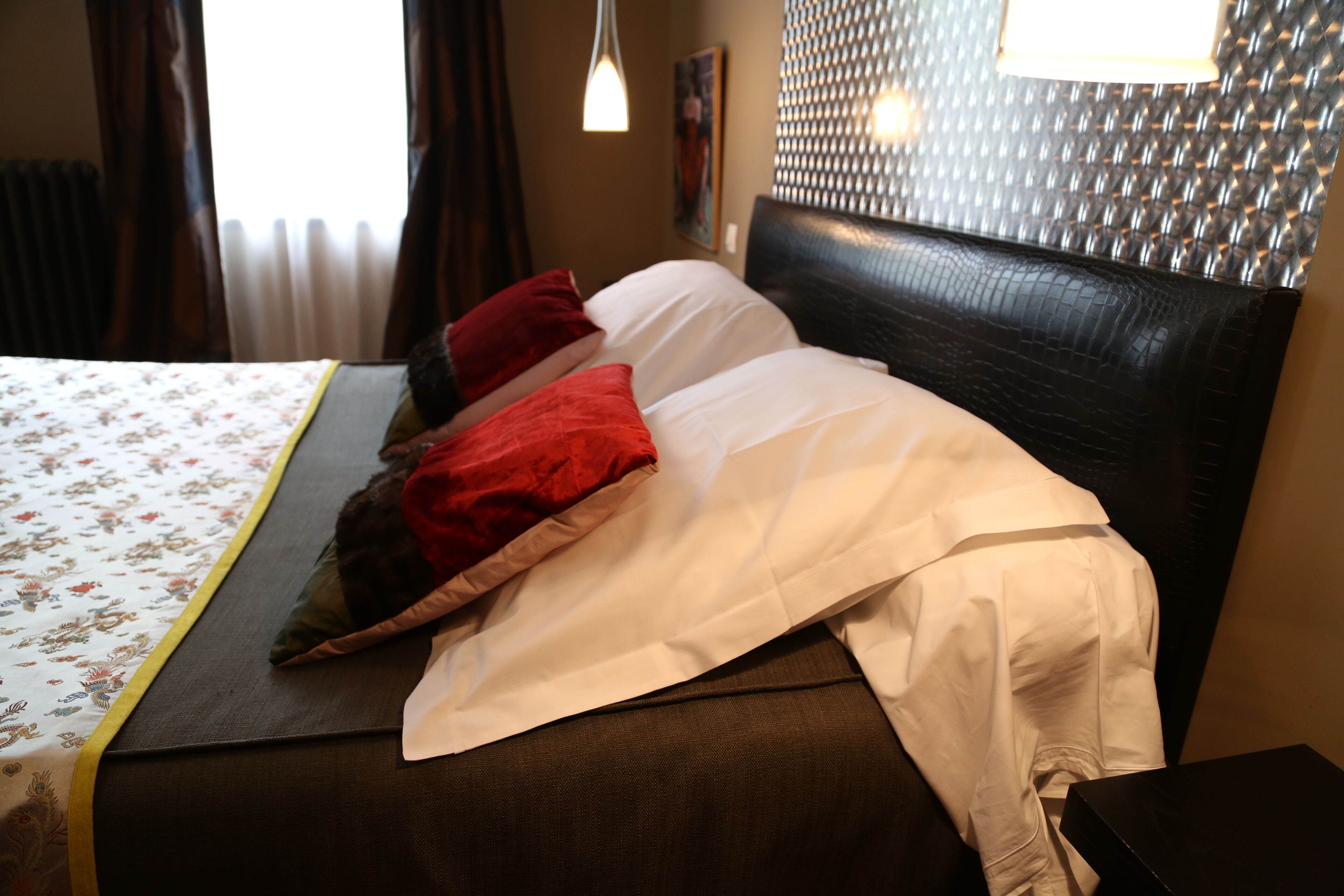 A neatly made bed with a floral bedspread, a headboard with a textured pattern, and a bedside table with a lamp.