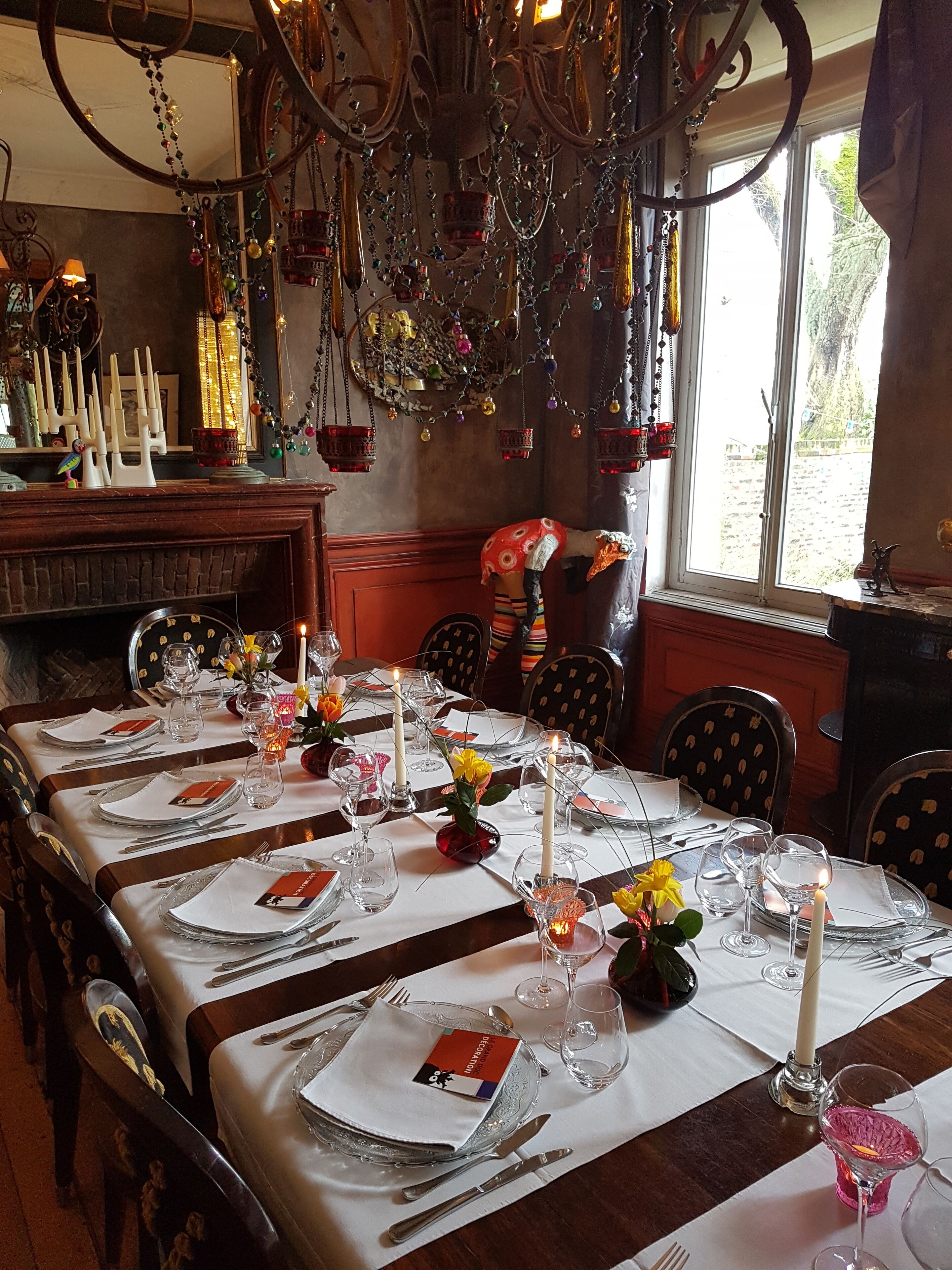 Uma sala de jantar com uma mesa comprida posta para uma refeição, com copos transparentes, pratos e velas.