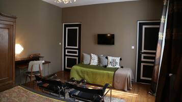A bedroom with a bed, a desk, a chair, a television, and a chandelier.