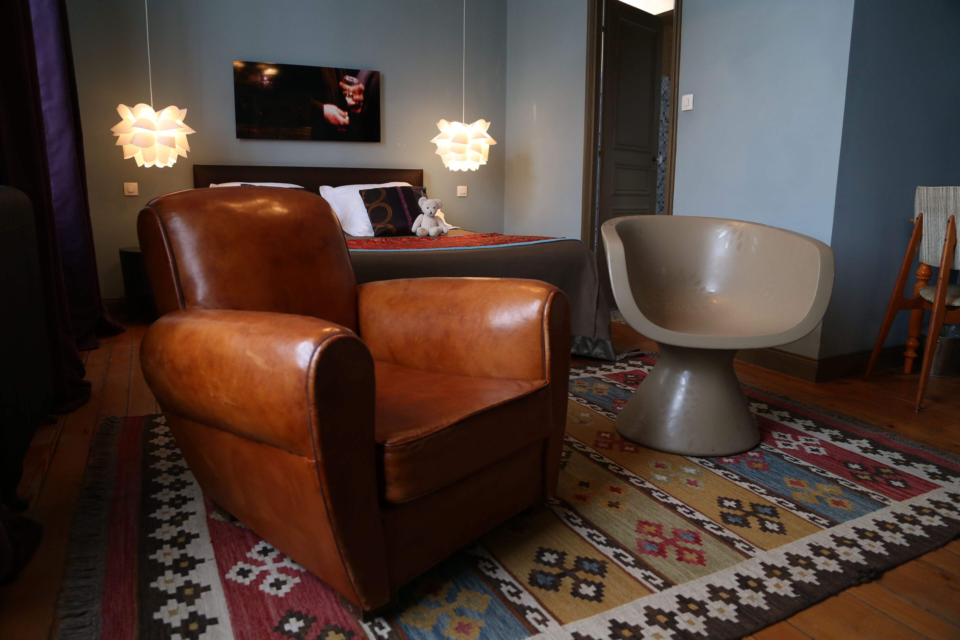 A room with a brown leather chair, a modern armchair, a patterned rug, and two hanging lamps.