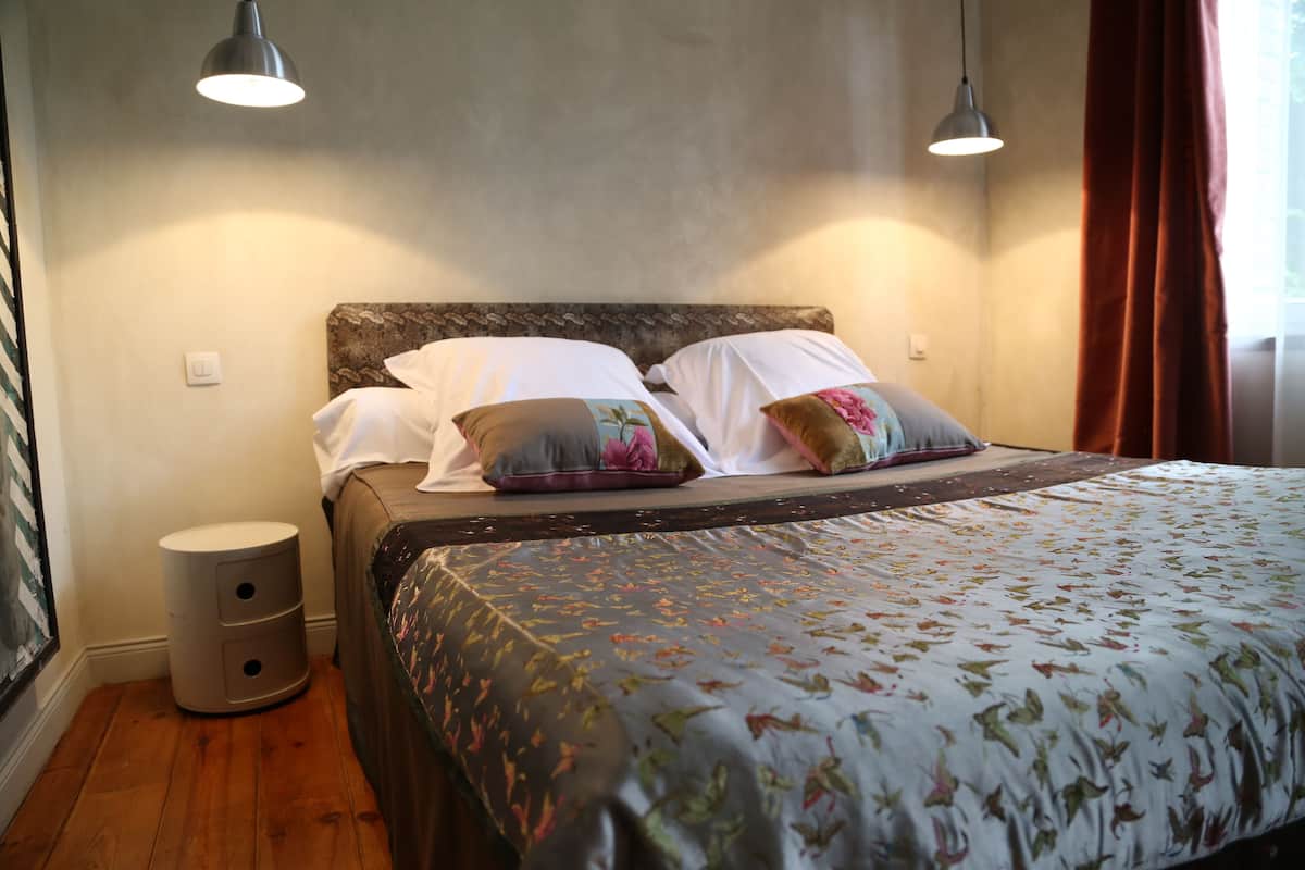 A bedroom with a bed, two bedside lamps, a nightstand, and a window with curtains.
