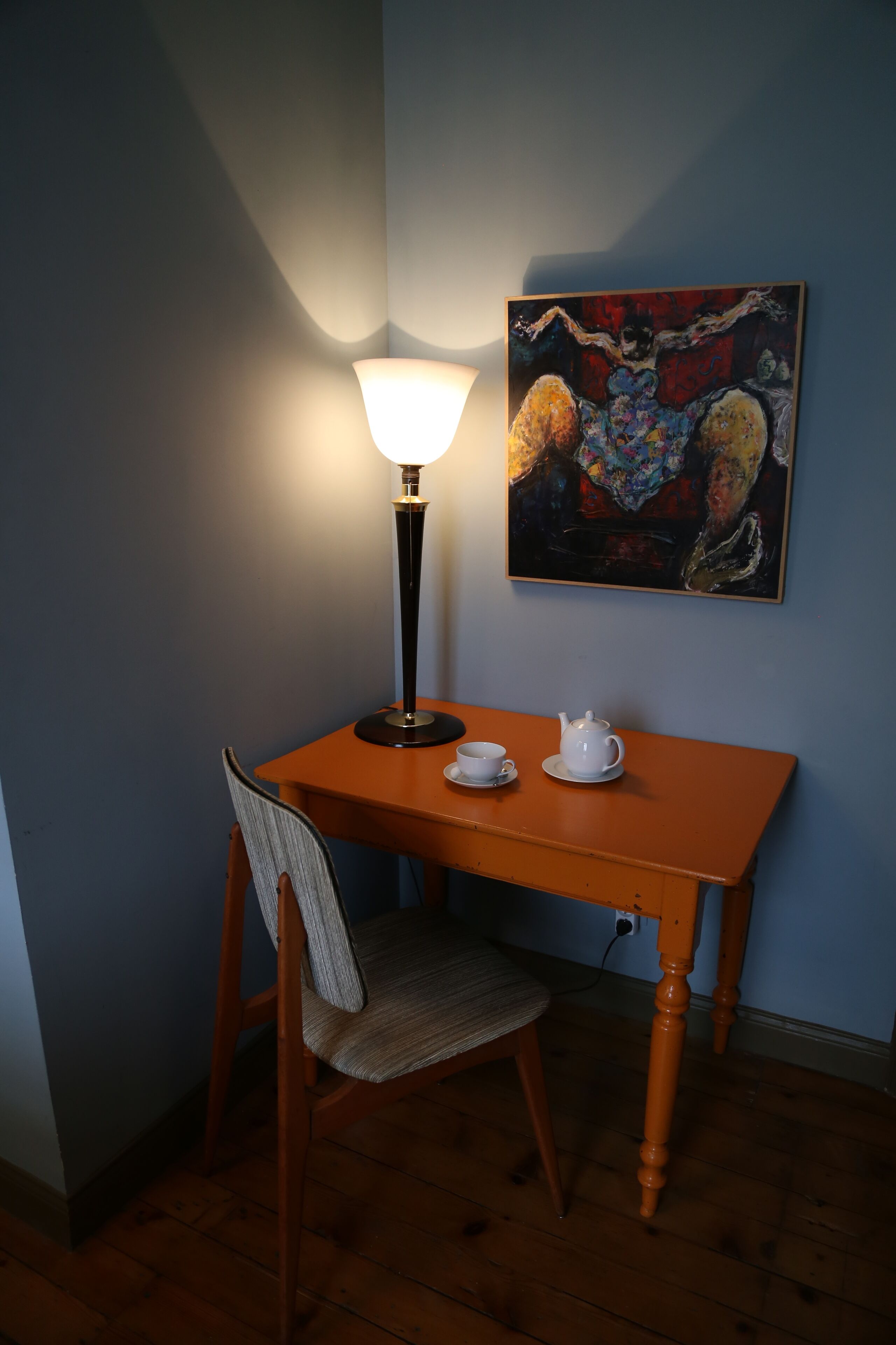 A small dining area with a table, a chair, a lamp, and a painting on the wall.