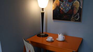A small dining area with a table, a chair, a lamp, and a painting on the wall.