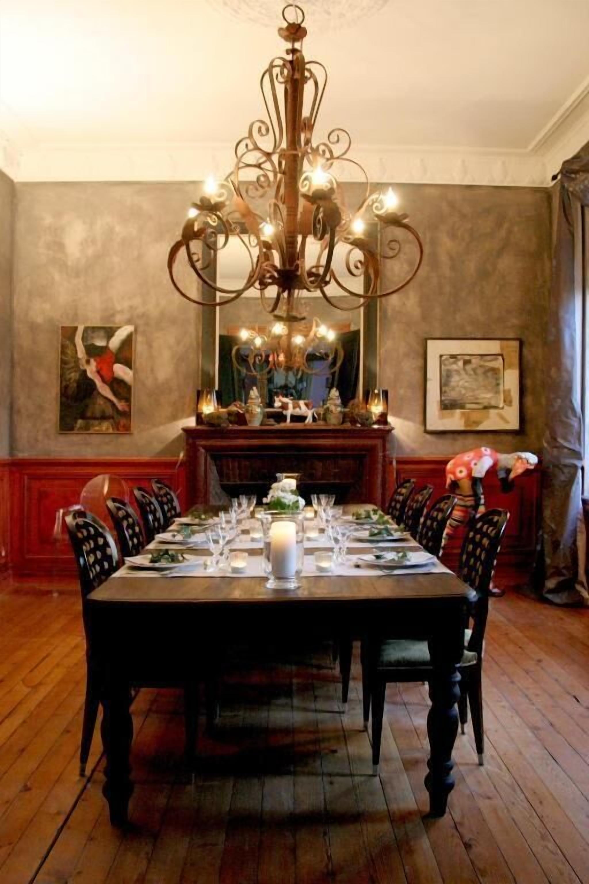 A dining room with a large wooden table set for six, a chandelier, and artwork on the walls.