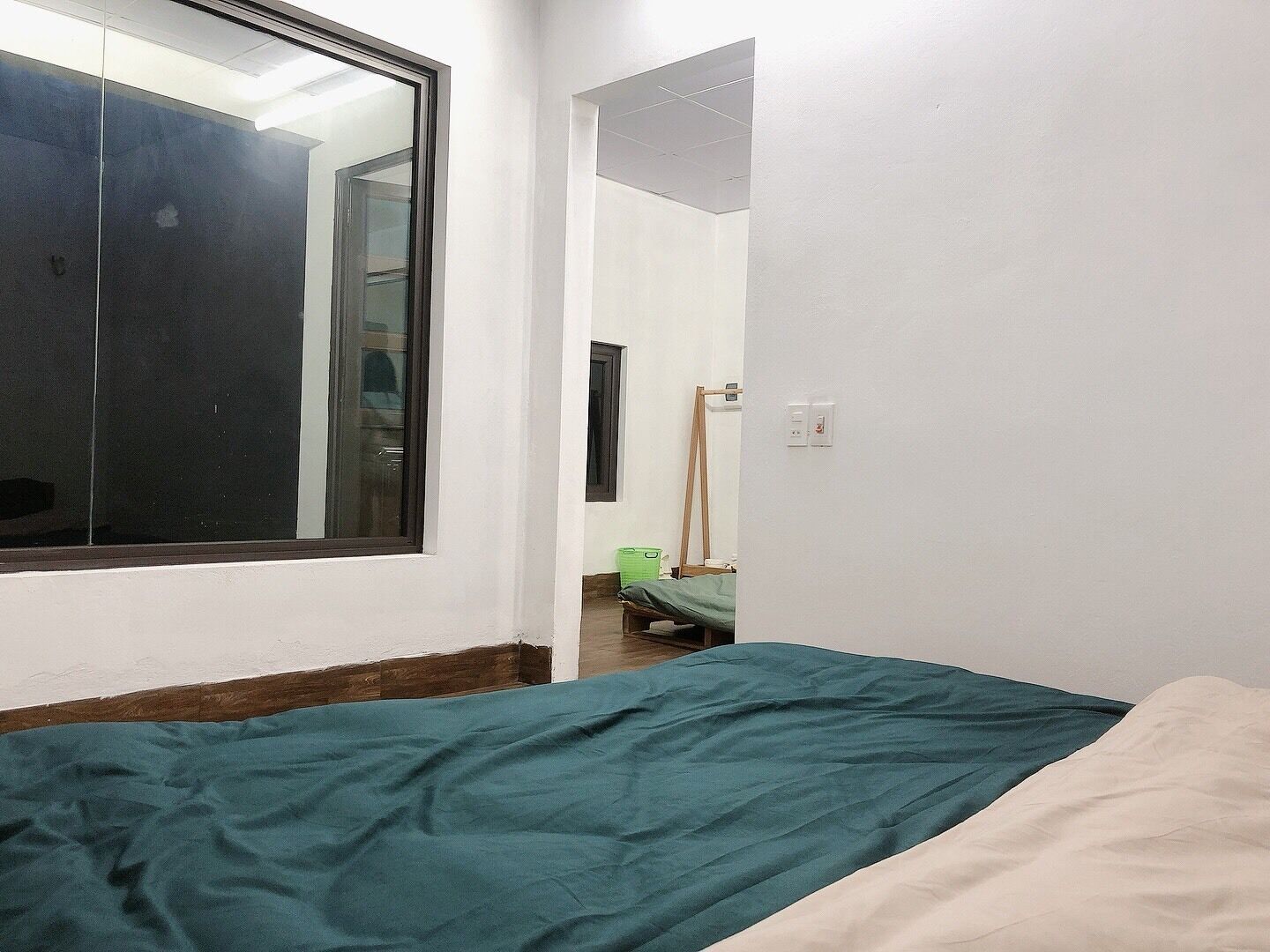 A small, narrow room with a single bed, a window, and a door leading to another room.