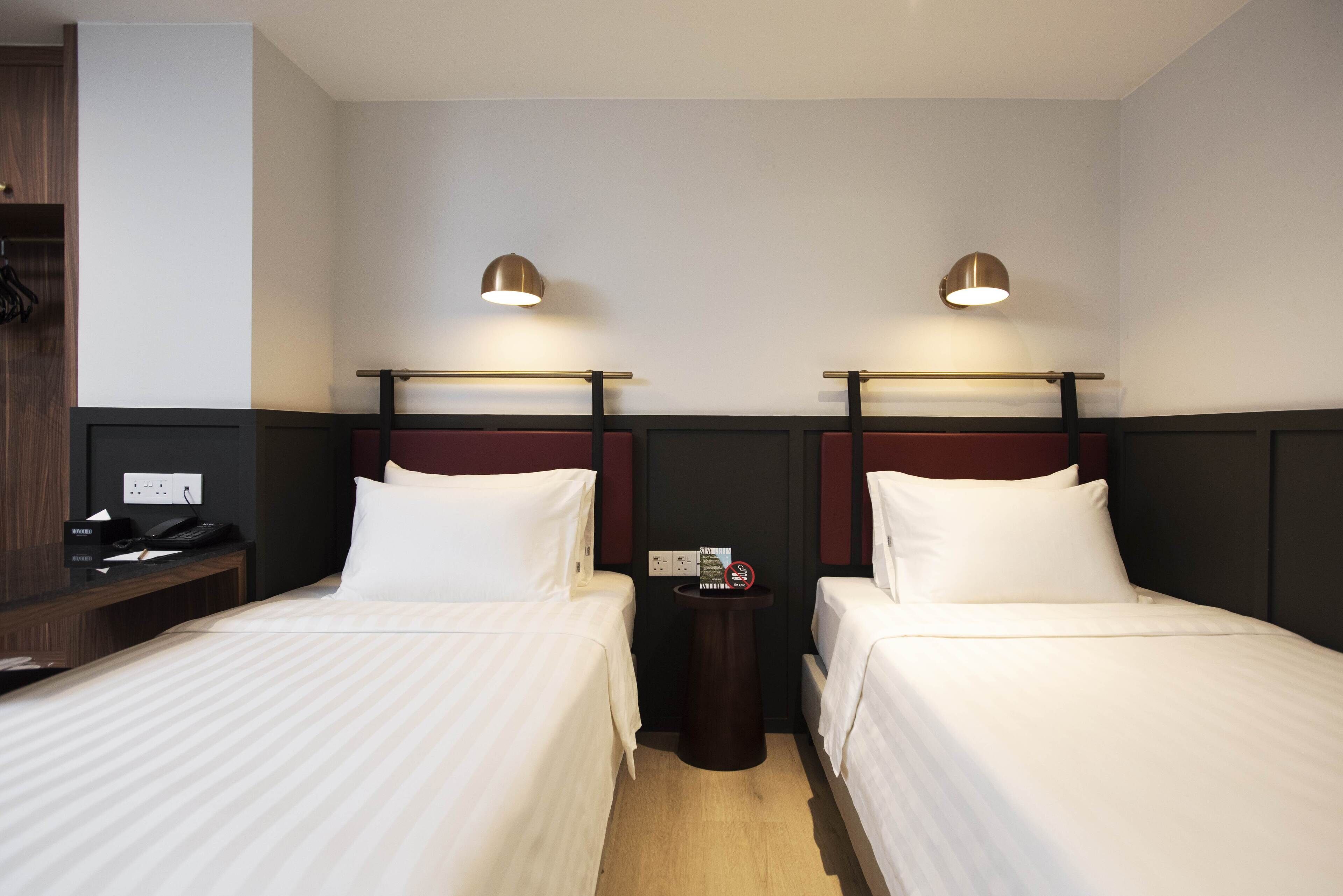 A hotel room with two beds, a small table, a telephone, and a wall socket.