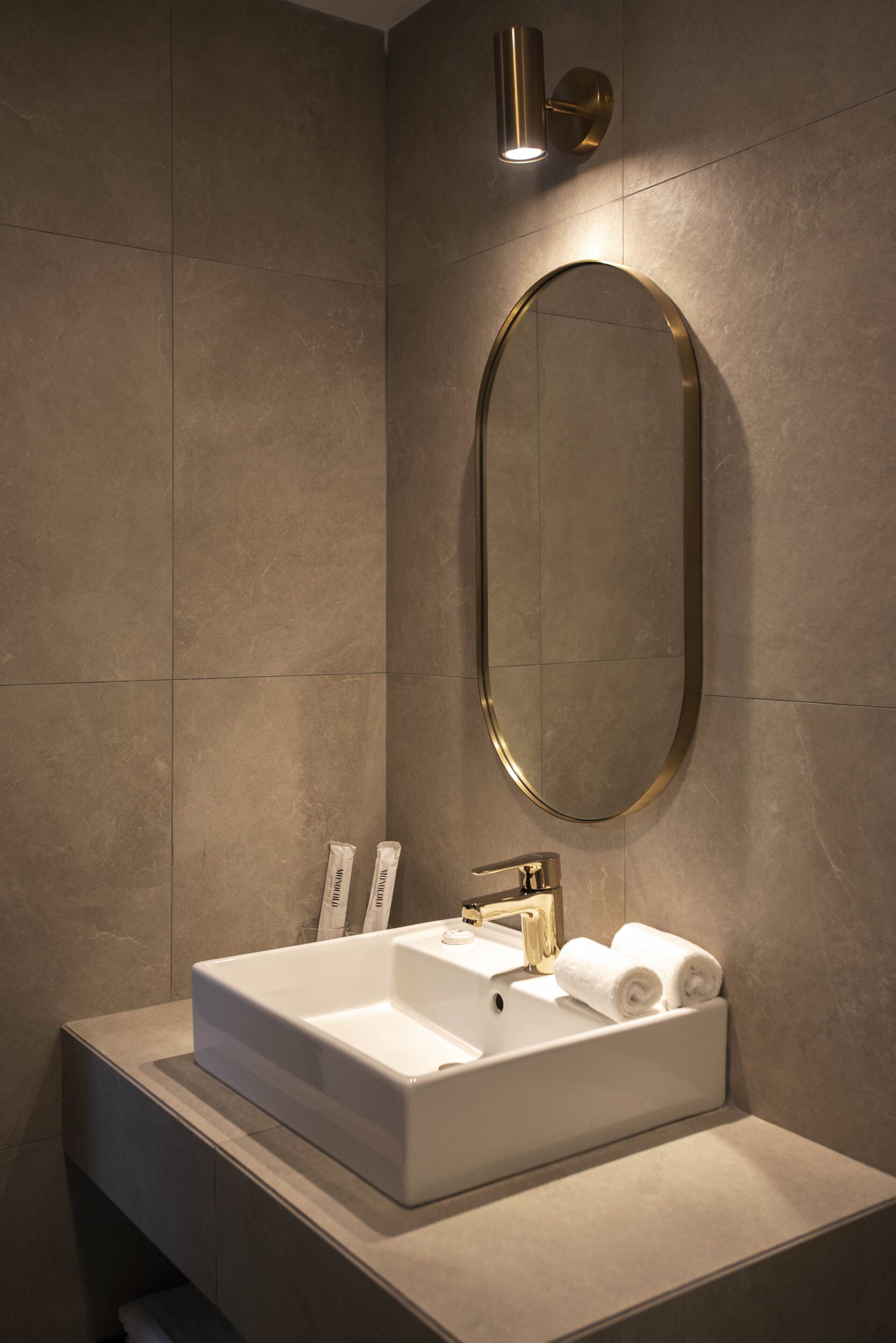Un baño moderno con un lavamanos rectangular, un espejo con marco dorado y una lámpara de pared.