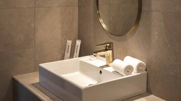Un baño moderno con un lavamanos rectangular, un espejo con marco dorado y una lámpara de pared.